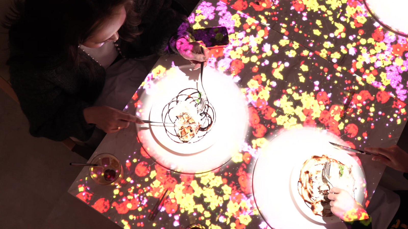 テーブル一面に広がる花のマッピングと、それを撮るゲストのスマホ（Little Chef Whitely）